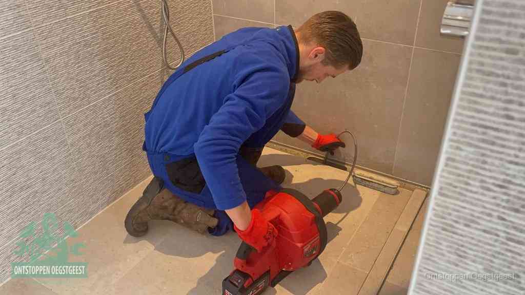 Een monteur ontstopt een langwerpige douchegoot met een elektrische veer, een doucheputje verstopt door haren en zeep in Oegstgeest