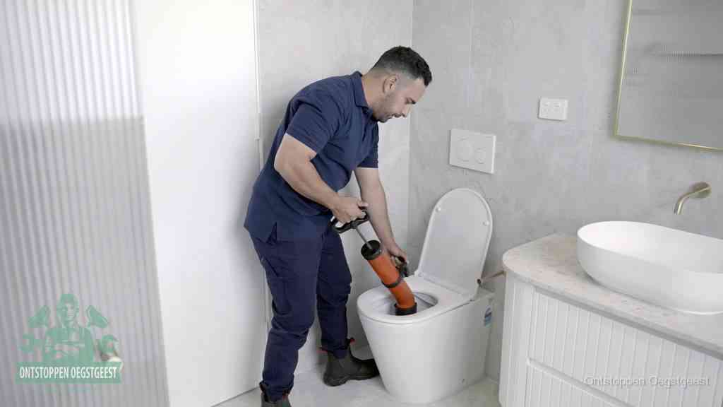 Een monteur buigt over een wandcloset en duwt met de hand een persluchtontstopper in de toiletpot om de verstopping handmatig los te maken in Oegstgeest