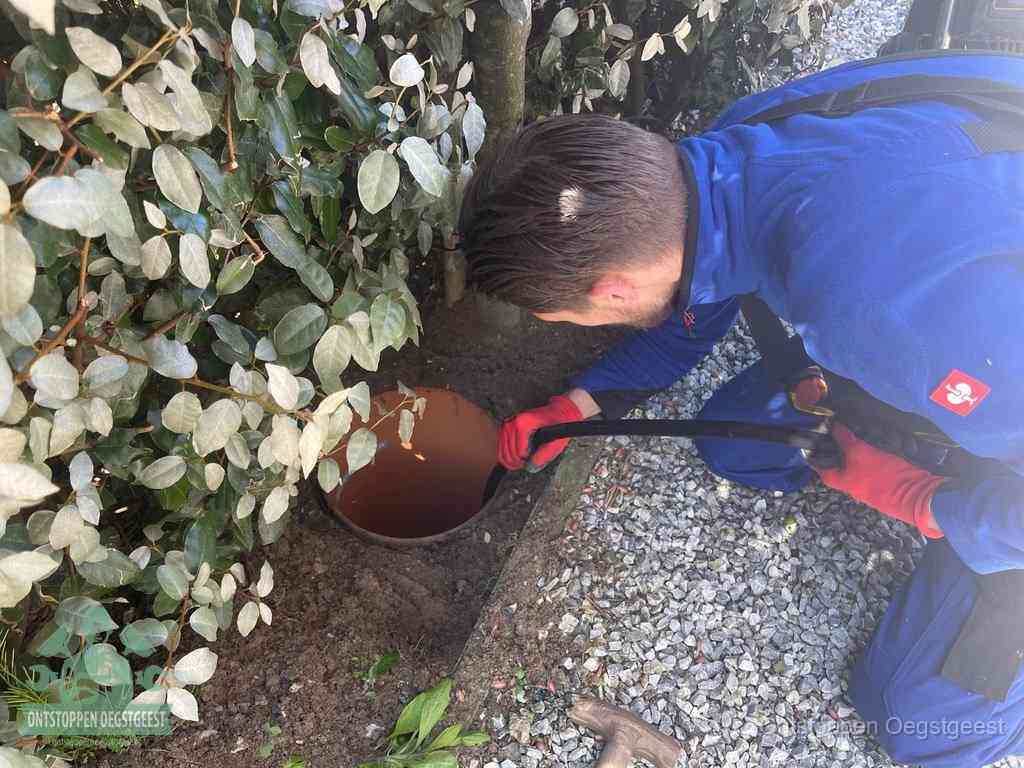 Een monteur voert een slang in een geopende rioolput in de tuin om het hoofdriool te ontstoppen in Oegstgeest