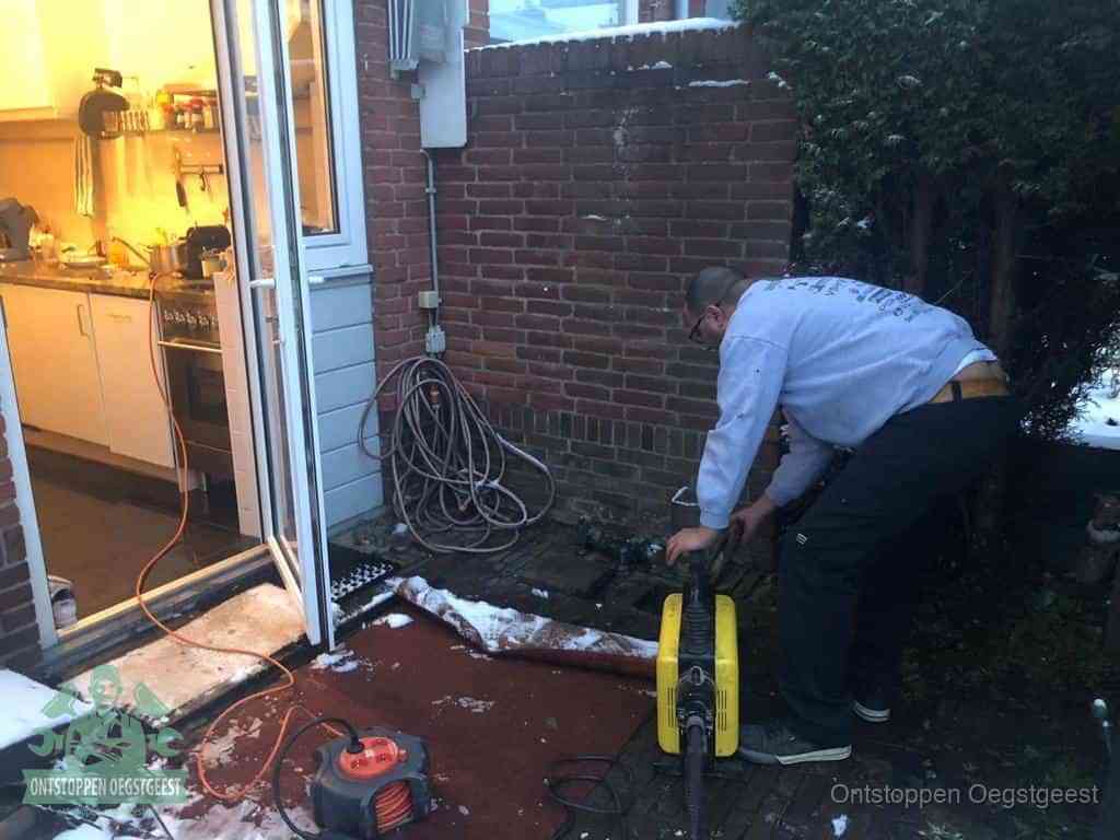 Een monteur werkt buiten bij een open riool-/grondput met een elektrische ontstoppingsmachine om een verborgen afvoerprobleem op te sporen in Oegstgeest