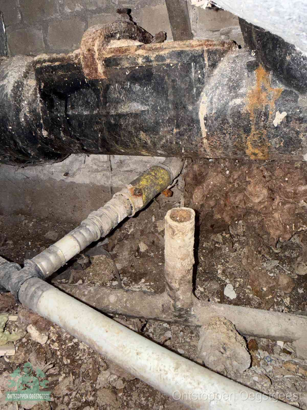 Een oude hoofdrioolbuis met roest- en kalkaanslag in een kruipruimte, oorzaak van terugkerende structurele rioolproblemen in Oegstgeest