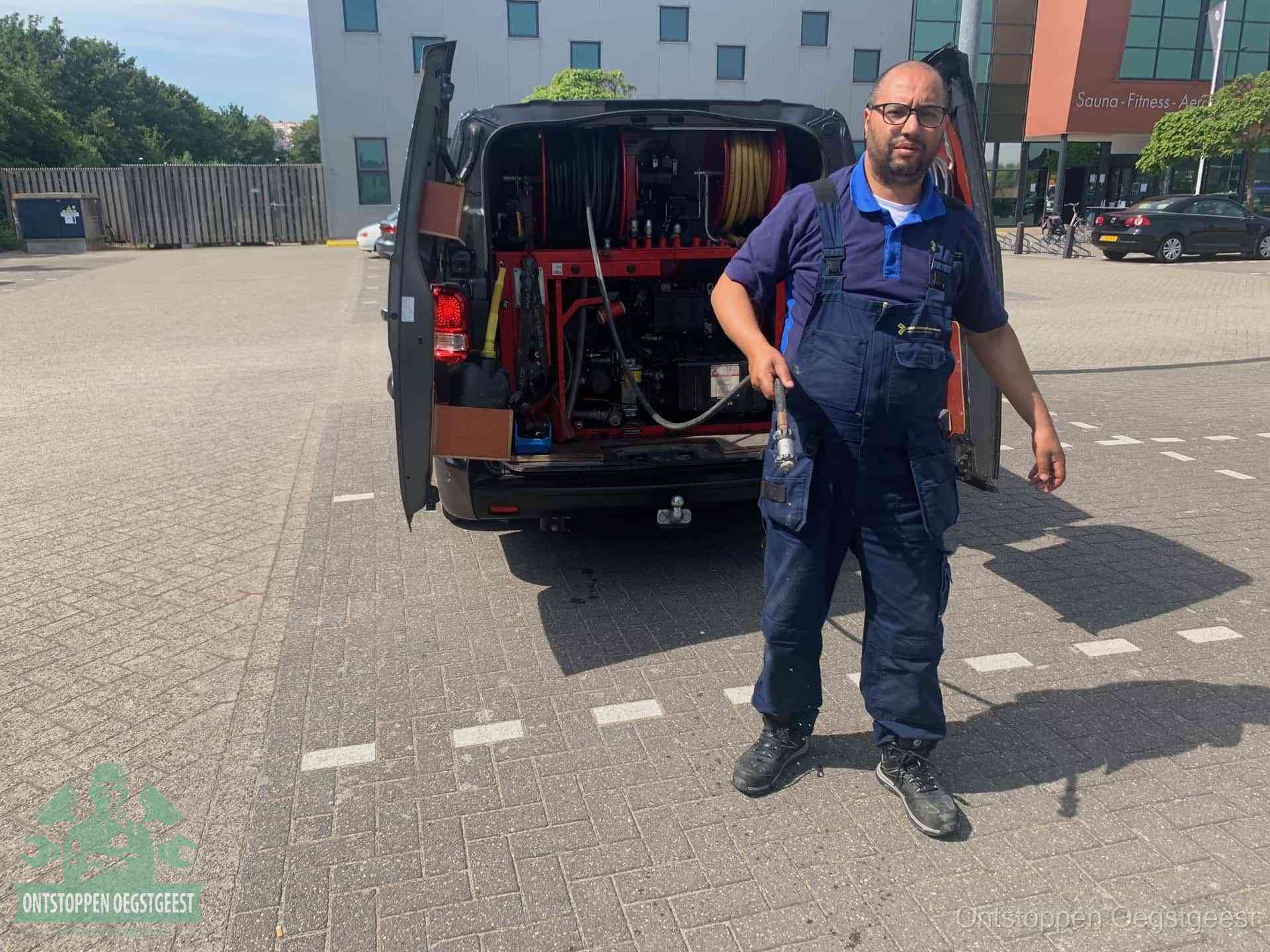 Een monteur bij zijn bestelbus met een hogedruk- en rioolreinigingsunit, klaar om de oorzaak van terugkerende wc-verstoppingen aan te pakken in Oegstgeest