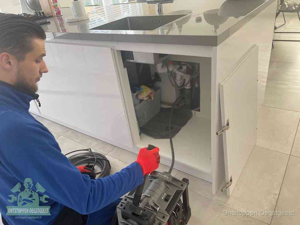 Monteur ontstopt met een veermachine een verstopte afvoer onder de gootsteen in Oegstgeest