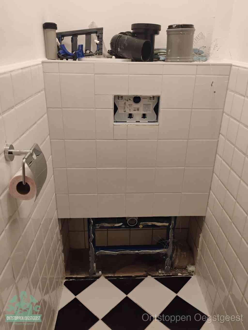 Een toiletruimte waar het hangtoilet en de inbouwreservoir-onderdelen zijn vrijgelegd voor onderhoud, periodiek nazicht voorkomt een wc-verstopping in Oegstgeest